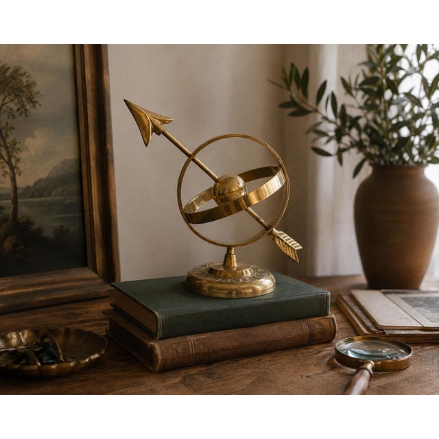 Vintage brass armillary sphere featuring an arrow passing through a circular celestial globe form on a decorative pedestal...