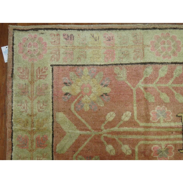 One of a kind Khotan rug with a soft pink field consisting of a flower vase motif and a soft green border.