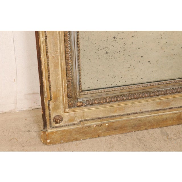 A French neoclassic carved and painted wood trumeau mirror from the 18th century. This antique mirror from France has the...