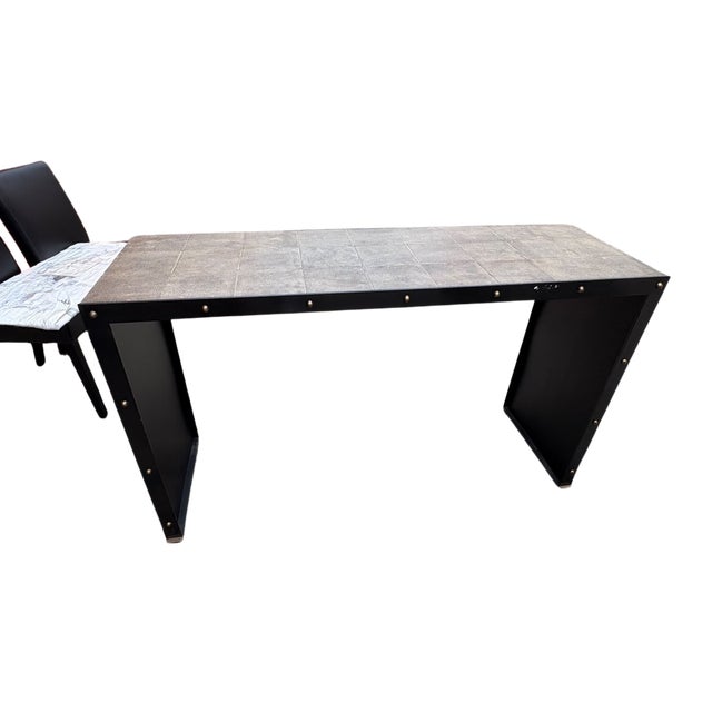 This striking console table features a sleek dark metal frame with decorative brass stud accents and a wood-tone surface...