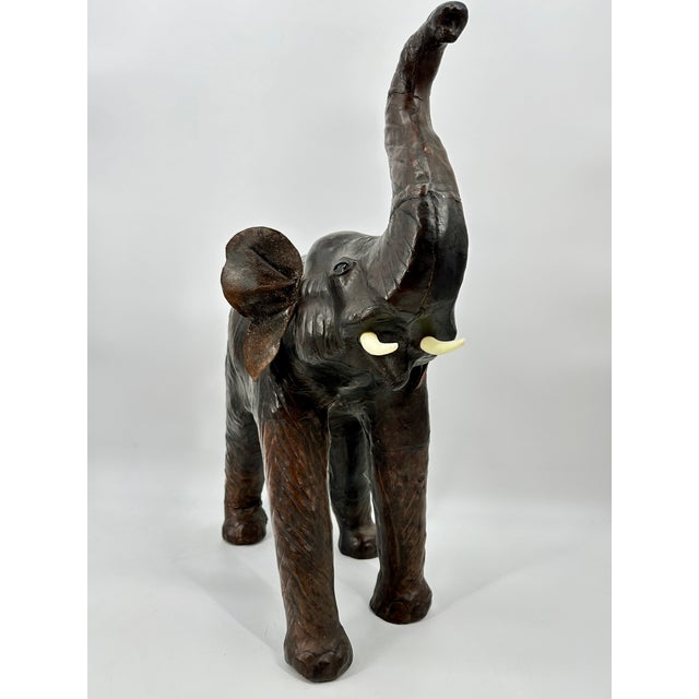 Beautifully aged large leather covered elephant with raised trunk. Glass eyes, standing tall. The tusks are made of molded...