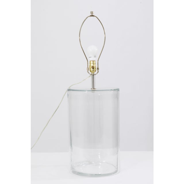 A sleek and understated modern table lamp featuring a substantial clear glass cylindrical base constructed in a two-piece...