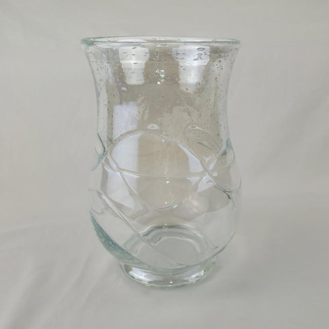 Hand-blown clear glass hurricane vase featuring a unique seeded texture and raised swirl ribbon detailing. This elegant...