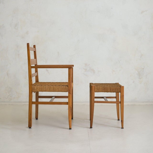 A 1950s French armchair and ottoman, crafted in solid wood with a handwoven rope seat. The frame is defined by its honest...