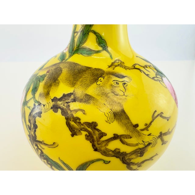 A striking vintage Chinese porcelain bottle vase decorated with a playful monkey among fruiting peach branches. The finely...