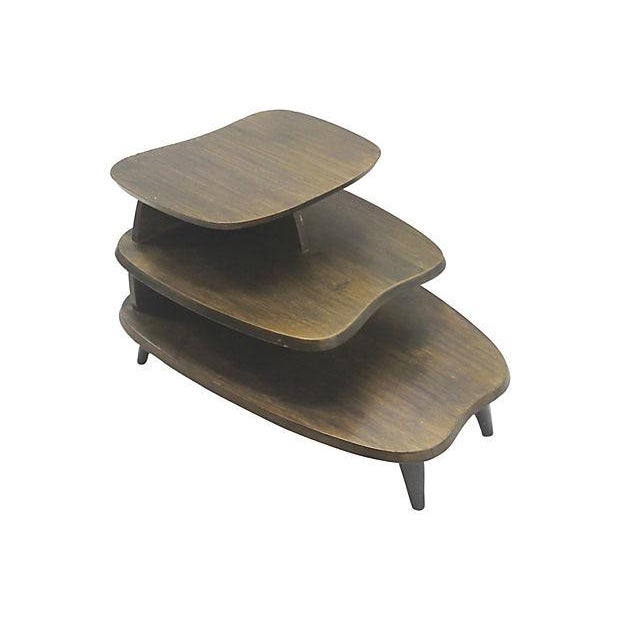 A Mid-Century stepped end table with three, staggered tiers, bio-morphic form shelves, and wide tapered legs. The 1950's...