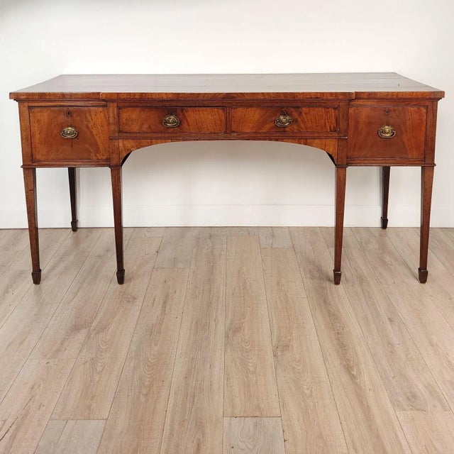 An English George III breakfront mahogany sideboard, circa 1800, standing on six square tapered legs with spayed feet.