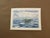 A serene original watercolor depicting a small green boat resting quietly on shimmering blue water beneath a softly...