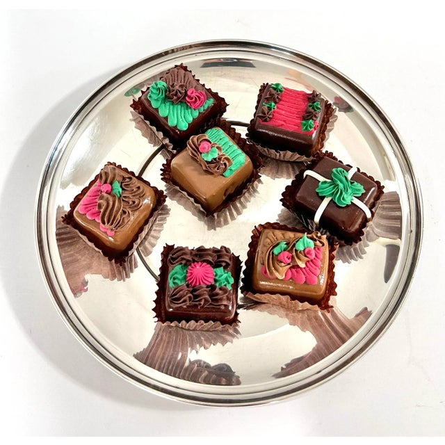 A charming vintage holiday display featuring seven highly realistic faux decorated chocolates arranged on a round...