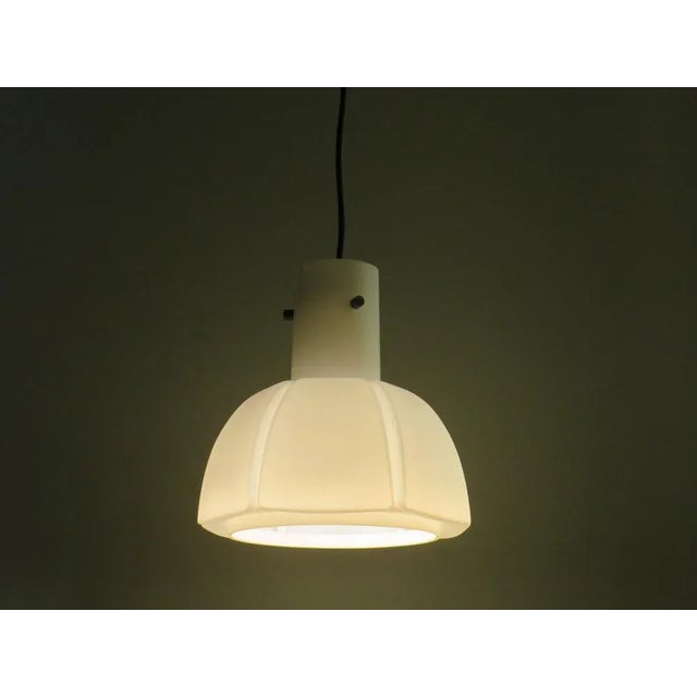 The lamp has a calyx shape made of thick white opaline glass and a metal socket with an E 27 fitting, which is fixed in...