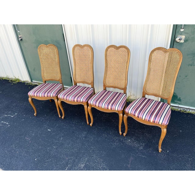 A set of four beautiful high cane backed and upholstered dining chairs in a French country style. Made from light fruit...