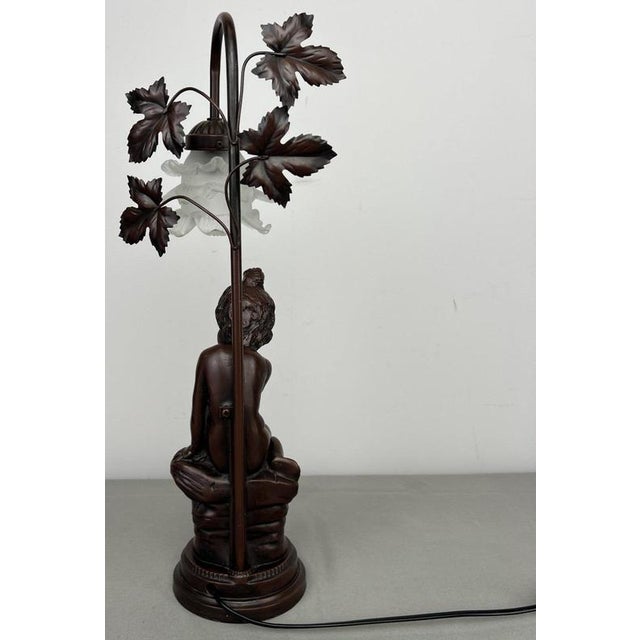 A decorative Vintage French lamp featuring a detailed seated female figure, an elegant curved upright and sculptural leaf...