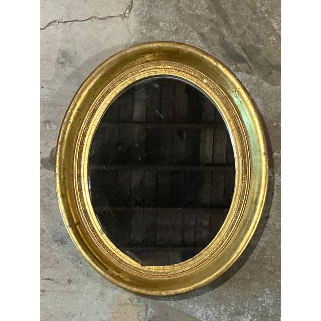 This antique oval wall mirror is an elegant testament to early 20th-century craftsmanship and refined design. The frame is...