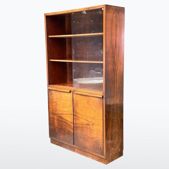 Art Deco bookcase from the 1930s, made of walnut veneer with a distinctive wood grain. Upper section with sliding glass...