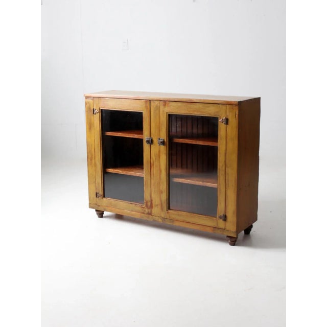 This is an antique display cabinet. The primitive wooden curio cabinet features double glass paned doors with three...