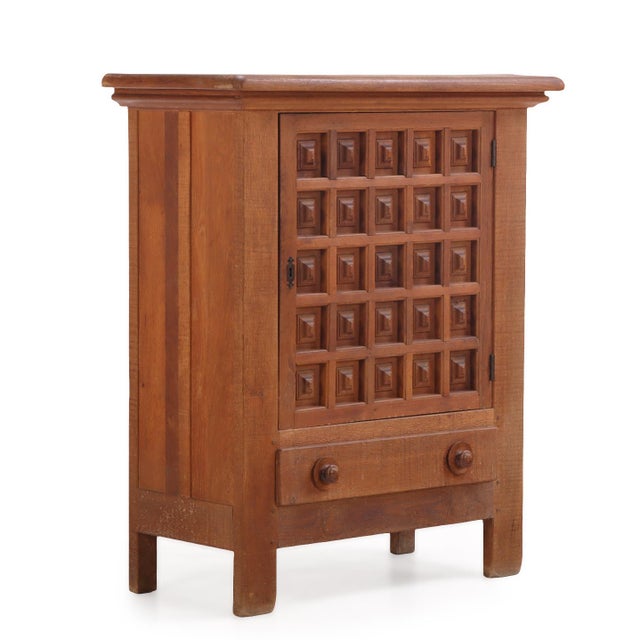 This cabinet having a single paneled door richly decorated with a grid of 25 deeply recessed, geometric square panels,...