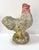 A weathered terracotta rooster garden statue with moss, mineral deposits, and softened surface texture from years...