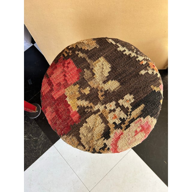 A round wood stool upholstered with a vintage kilim wool carpet remnant