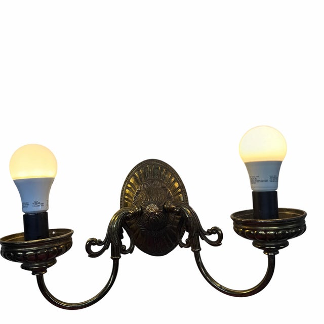 Vintage brass two light electric wall sconce. The two arms boast a lovely shape coming from the ornate center medallion...