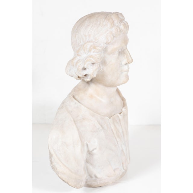 Hand carved, marble bust in three quarters, of a young man in a sensitively rendered, open-neck robe, with flowing hair...