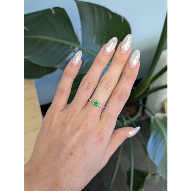 A natural tsavorite garnet from Tanzania brings electric green brilliance to this round ring, framed by sparkling diamonds...