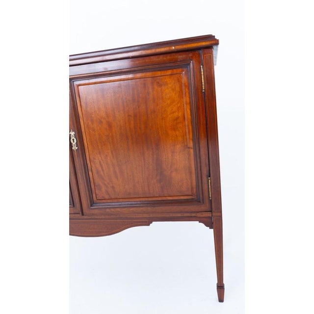 An elegant Sheraton Revival mahogany two-door cabinet, raised on square tapered legs terminating in spade feet The shaped...