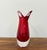 A sculptural Murano-style art glass vase featuring a vivid ruby-red interior encased in thick clear glass. The substantial...