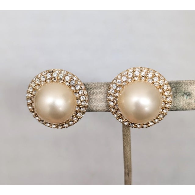 1980s goldtone round faux-pearl center with pavé round clear rhinestone clip earrings. Marked "CINER®" on the clips and...