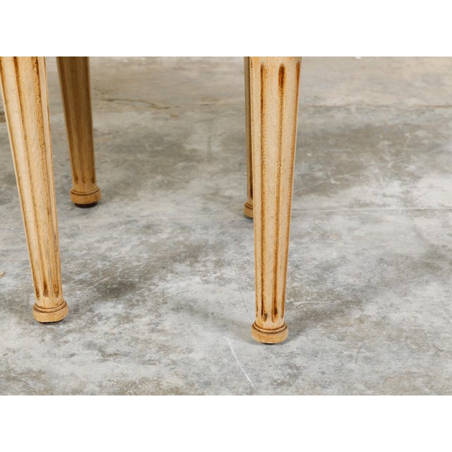 A pair of French neoclassical style bleached wood stools from the early 20th century, with fluted legs and new upholstery....