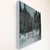 This oil painting captures a serene winter landscape, featuring a solitary red gate set against a backdrop of muted greens...