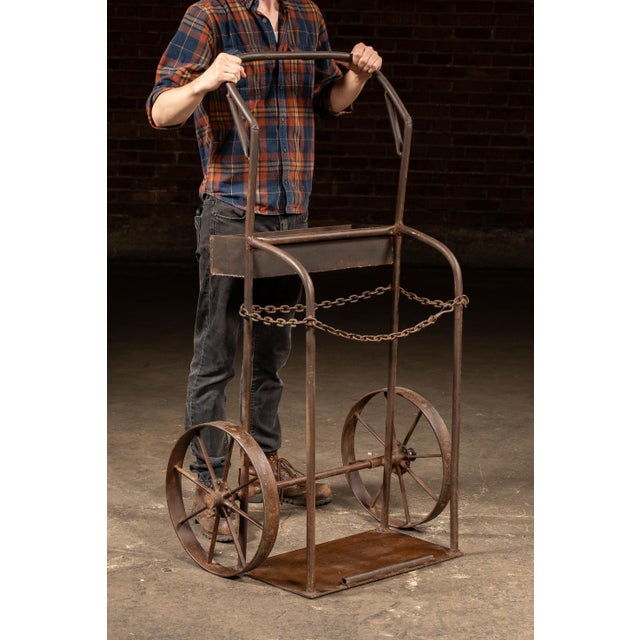 Riveted and welded steel cylinder cart featuring spoked cast-iron wheels, a curved handle frame, and an original safety...