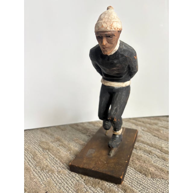 A whimsical carved wooden ice skater mounted on a rectangular wooden base, carved from one piece of wood with a great...