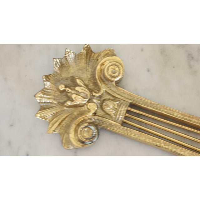 An ornate vintage lacquered brass wall sconce featuring a classical lyre or harp-form backplate with four slender...