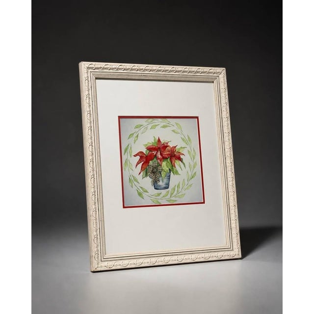 Decorative framed floral wall art featuring red poinsettia-style flowers in a blue pot with a soft green leaf wreath...