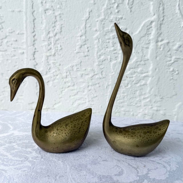 A graceful pair of vintage brass swan sculptures showcasing elegant Art Deco-inspired silhouettes and a naturally aged...