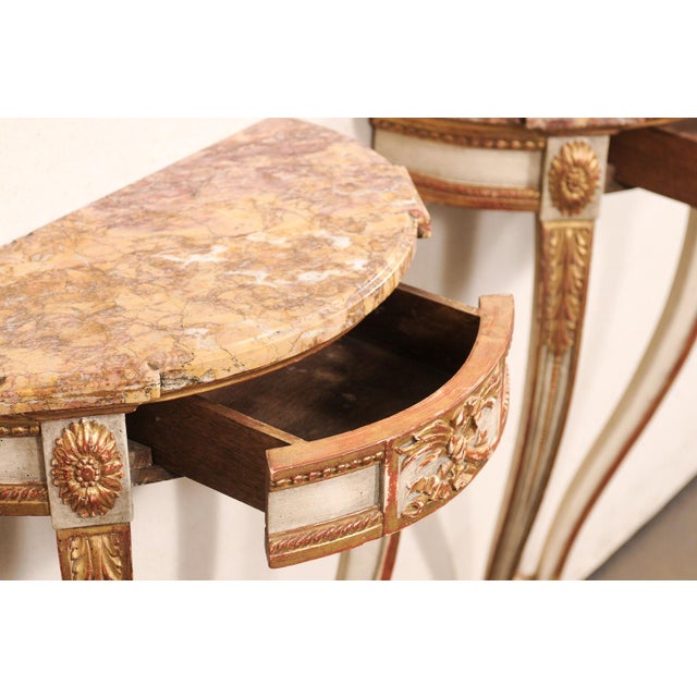 A French pair of carved wood demi-lune wall console tables, with marble tops, from the mid 20th century. These vintage...