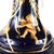This is a large dark blue jar or vase with a matching lid. It has a gold design of angels, harps, vases, and arrows. The...
