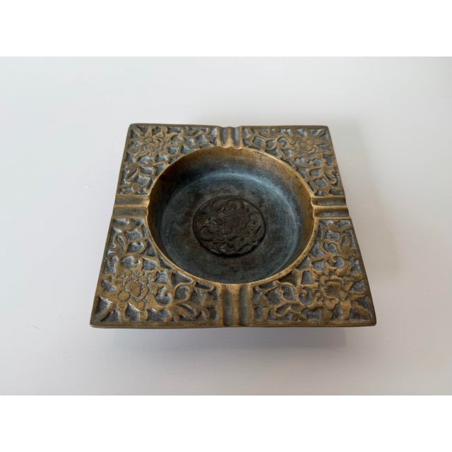 Vintage solid brass ashtray featuring an elegant square form with an ornate floral and scrolling relief pattern...