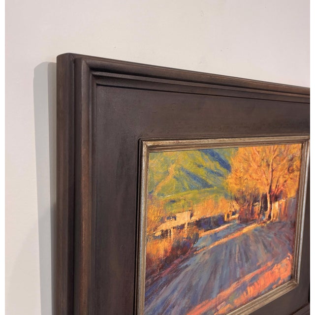 The painting captures a tranquil late afternoon scene at Taos Pueblo, where warm sunlight bathes the landscape in golden...