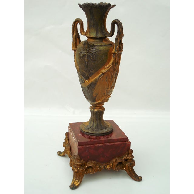 An elegant decorative urn in the Neoclassical style, featuring relief floral motifs and ornate scrolled handles. The...