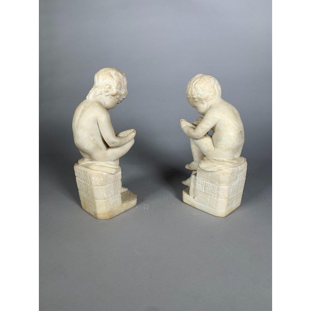 Two 19th-century white marble sculptures depicting a child scribe and a child reading, after Lemire (Charles Gabriel...