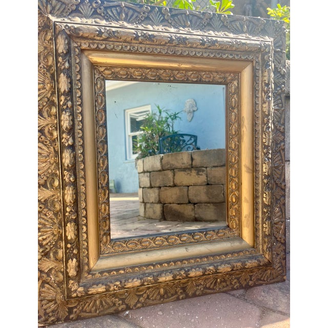Antique wall mirror with intricate raised border designs in gold with tones of black.