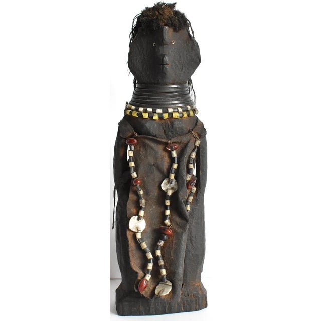 An African Dinka Doll. Hand-carved from wood, with wool hair, a leather dress, and trade bead details. Inset glass bead...
