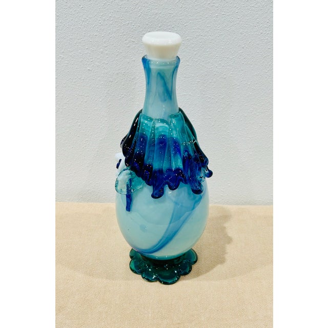 Vintage hand blown glass decanter in various shades of blue and white on a teal ruffled base. Includes original white...
