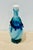 Vintage hand blown glass decanter in various shades of blue and white on a teal ruffled base. Includes original white...