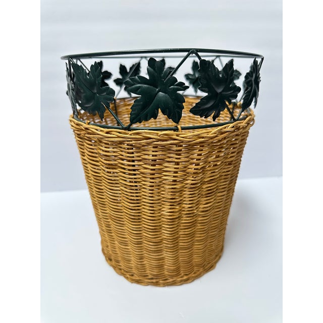 Vintage woven wicker waste basket with metal leaves accent. Measures 8 1/2” wide x 10 1/2” tall.
