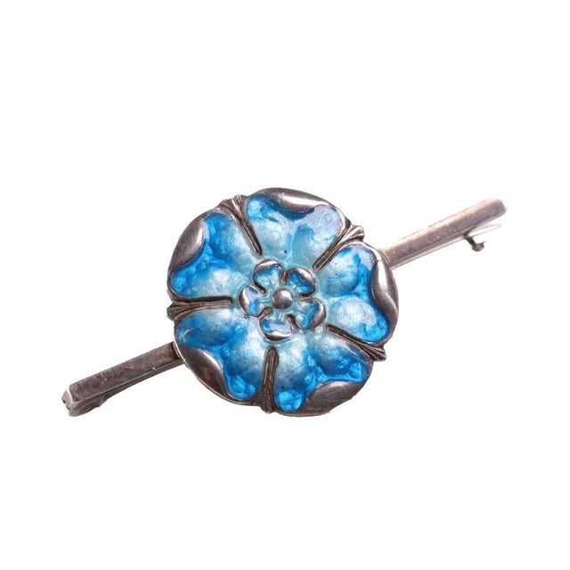 Shaded turquoise and pale sky-blue vitreous enamel fills the stylized Tudor rose plaque of this silver bar brooch. The...
