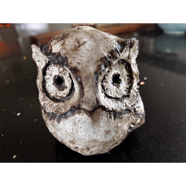 Handcrafted ceramic sculpture characterized by large eyes surrounded by pigments and a rough texture, probably made of...
