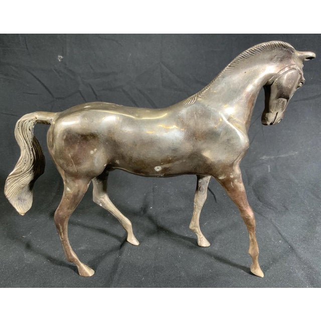 A brass horse sculpture in a walking pose with a smooth, polished body in a warm bronze tone reddish-brown patina or...