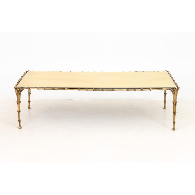 Maison Jansen Style Brass Coffee Table, with gold-washed beveled mirror glass top and floral motif frame. 15.5" H x 57.75"...